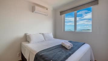 A bedroom with a bed, a window with a view, and an air conditioning unit.