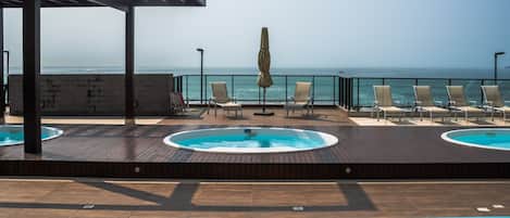 Un espace piscine aménagé sur le toit, avec des chaises longues et un jacuzzi, offrant une vue sur la mer.