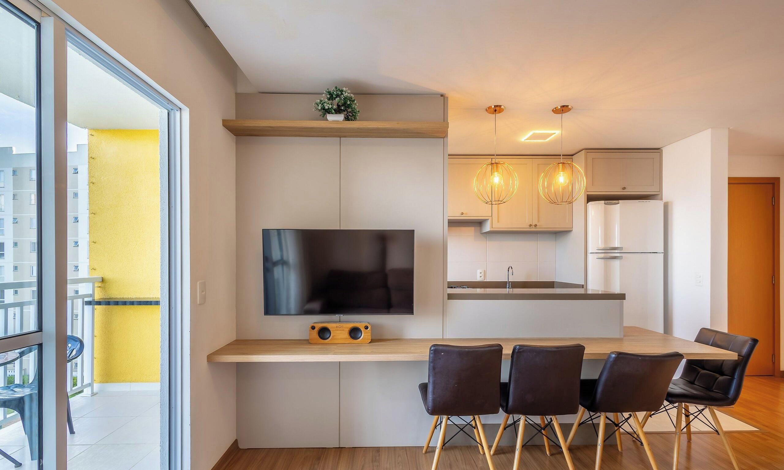 Une cuisine moderne équipée d’un téléviseur à écran plat, de meubles en bois, d’un coin repas avec des chaises et d’une petite plante posée sur le plan de travail.