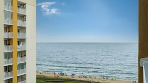 Vista costera con playa, océano y un edificio de varios pisos con balcones.
