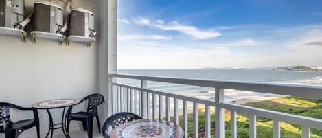 A balcony with a view of the sea, a round table, two chairs, and air conditioning units.