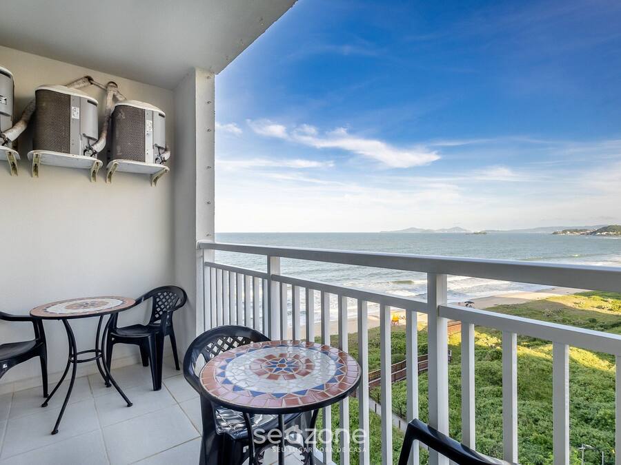 A balcony with a view of the sea, a round table, two chairs, and air conditioning units.