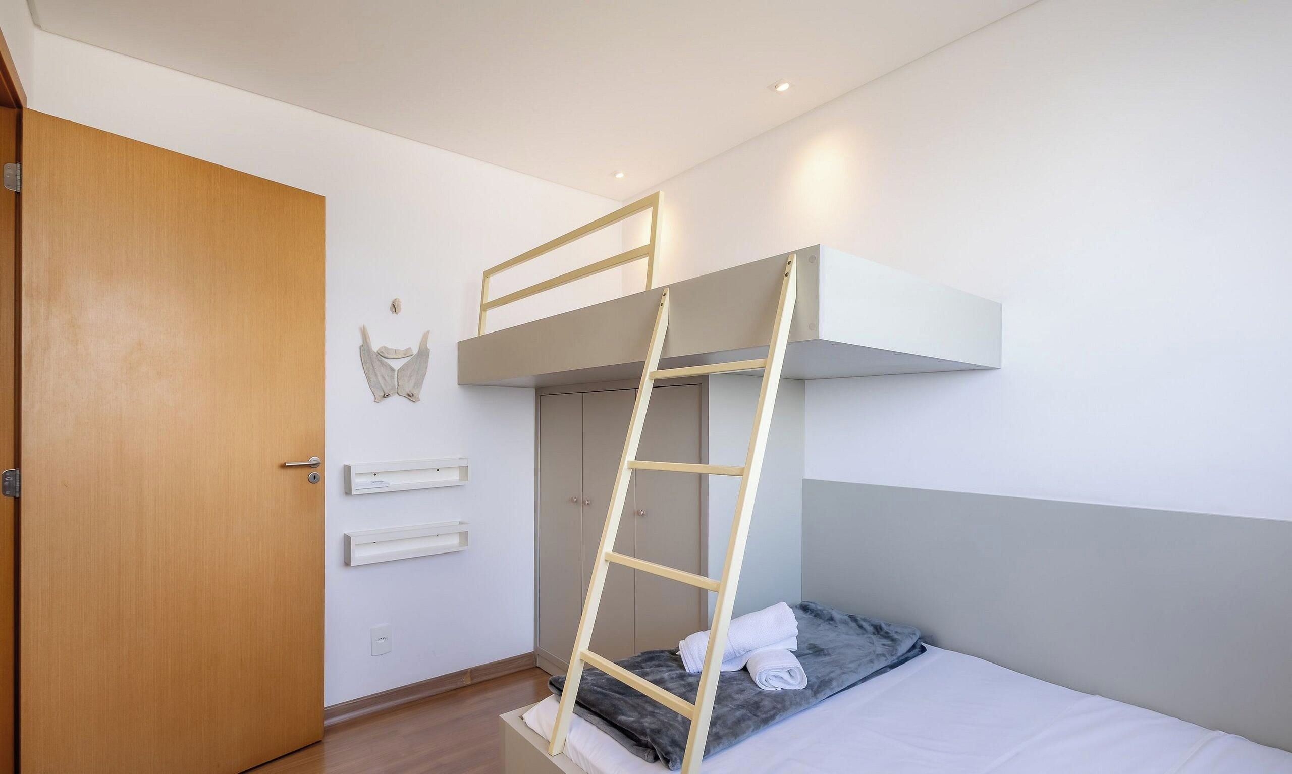 Una cama litera con escalera, una puerta de madera y una estantería fijada a la pared.