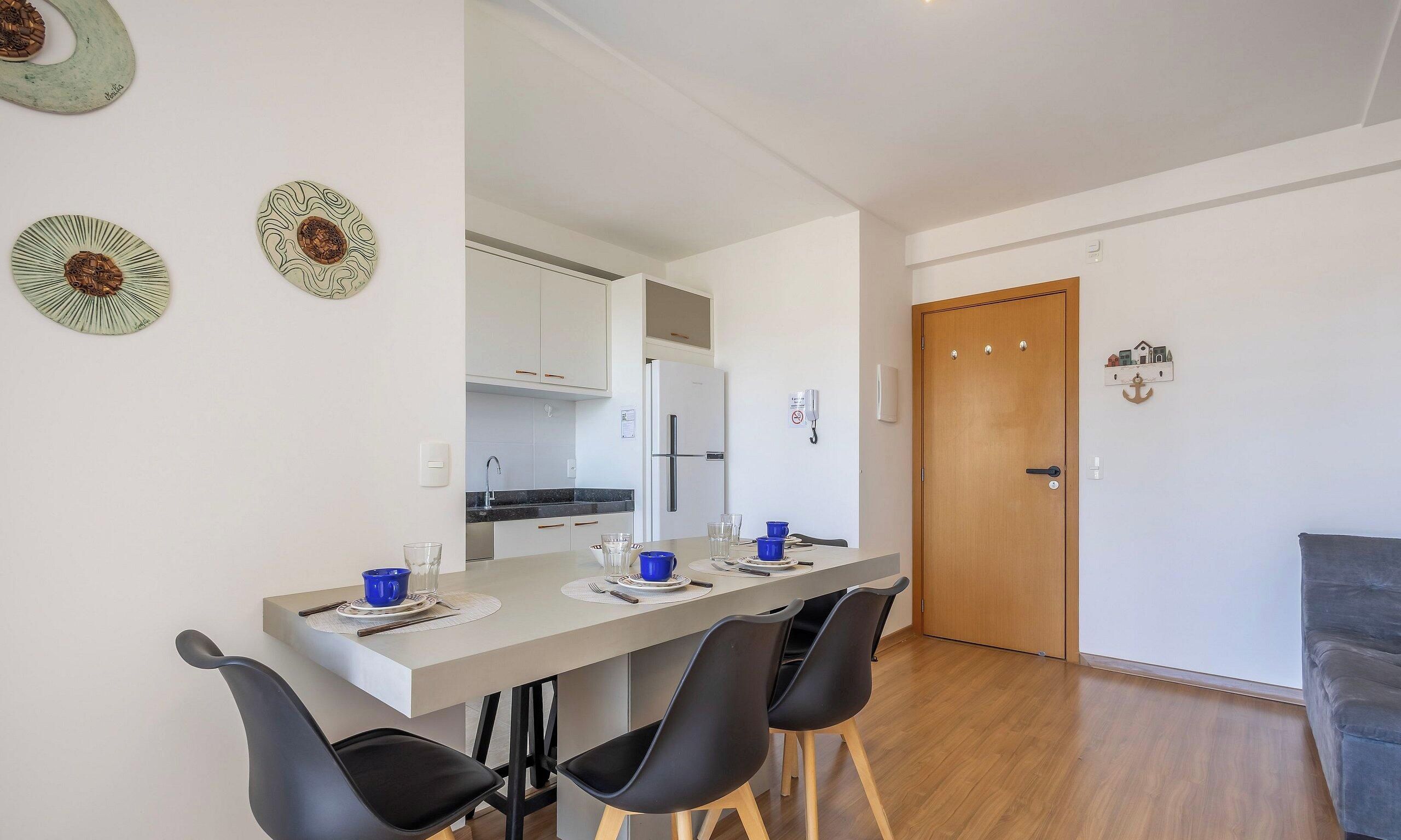 Una cocina moderna con armarios blancos, un refrigerador y un comedor con una mesa larga y cuatro sillas.