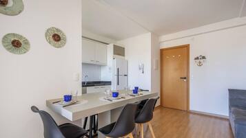 Una cocina moderna con armarios blancos, un refrigerador y un comedor con una mesa larga y cuatro sillas.