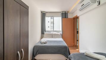 A bedroom with a bed, a wardrobe, a window with curtains, and an air conditioning unit.