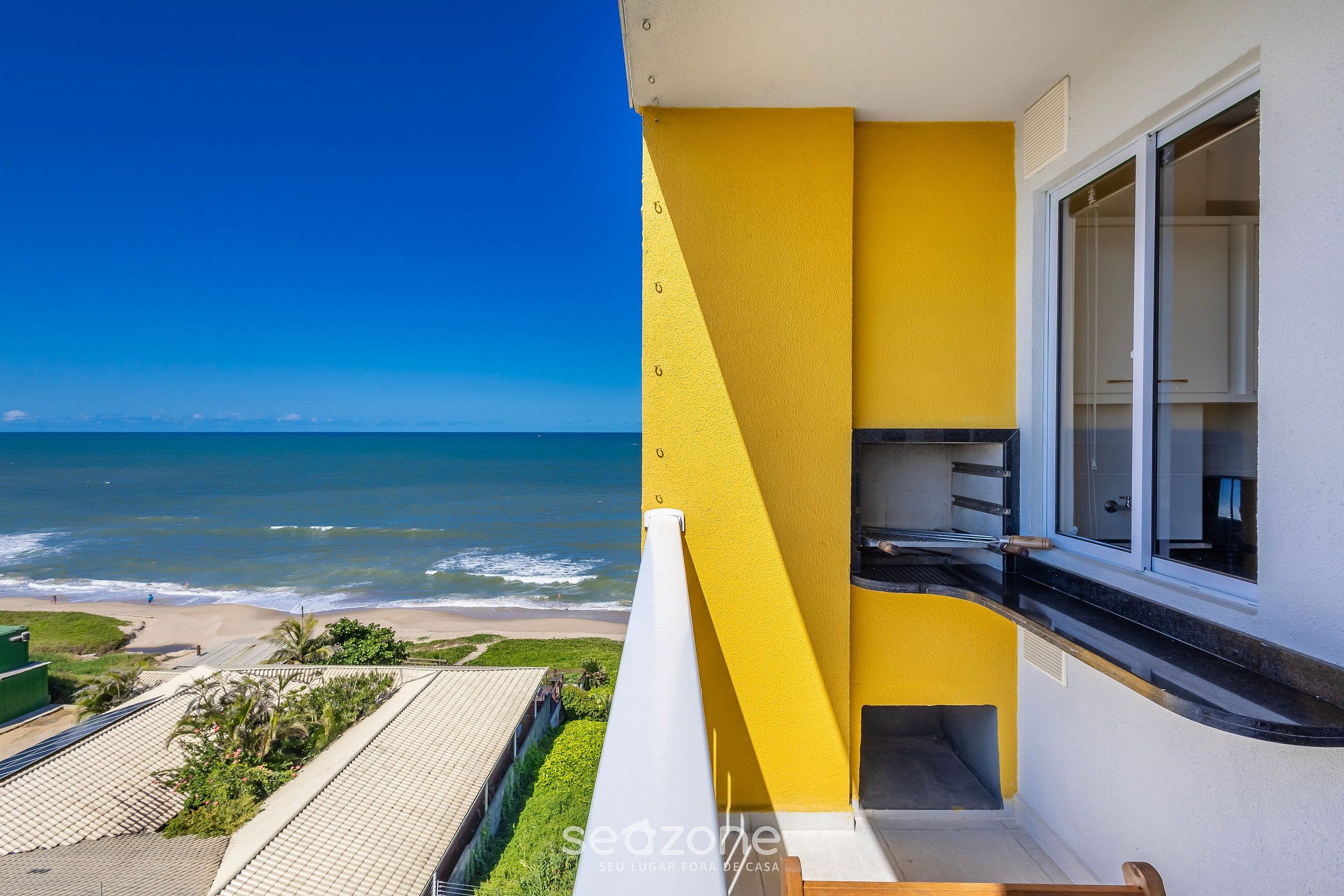 A balcony with a yellow wall, a view of the ocean, and a beach.