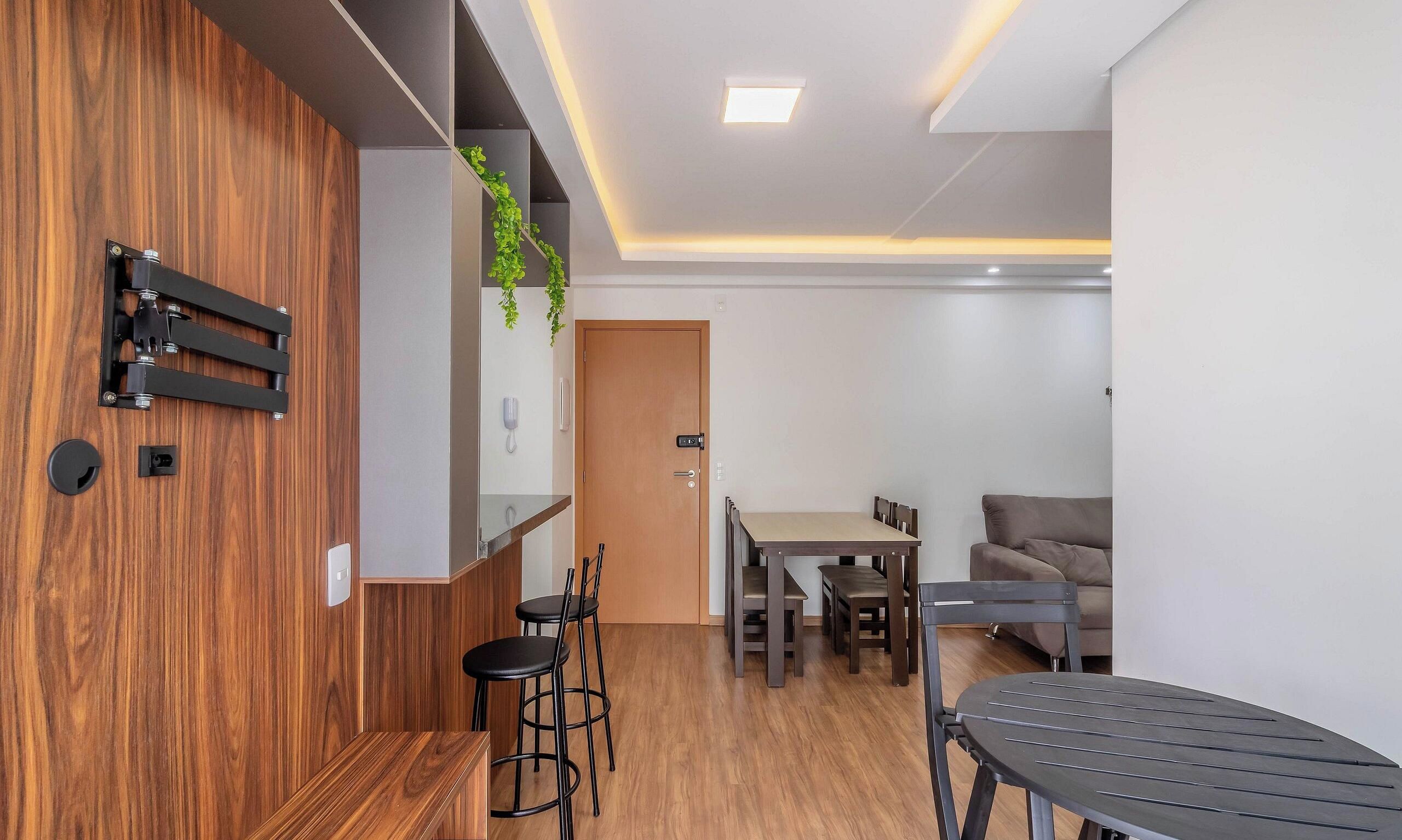 Un espacio habitable moderno con una pared de acento de madera, un comedor con mesa y sillas, un sofá y una pequeña cocina con refrigerador.