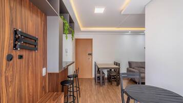 Un espacio habitable moderno con una pared de acento de madera, un comedor con mesa y sillas, un sofá y una pequeña cocina con refrigerador.