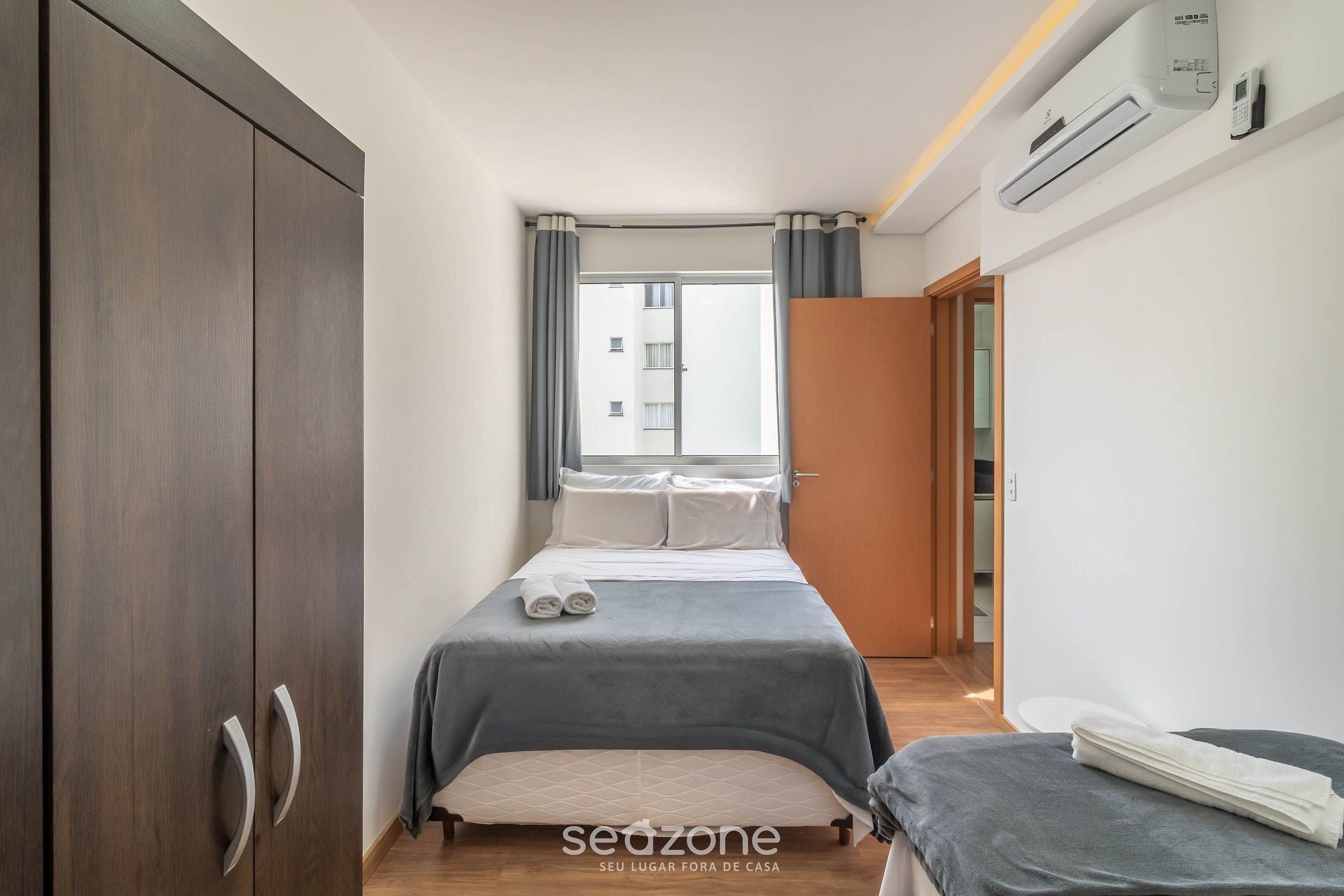 A bedroom with a bed, a wardrobe, a window with curtains, and an air conditioning unit.