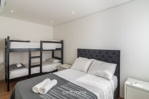 Un dormitorio con literas, una cama grande con cabecera capitonada y una mesita de noche.