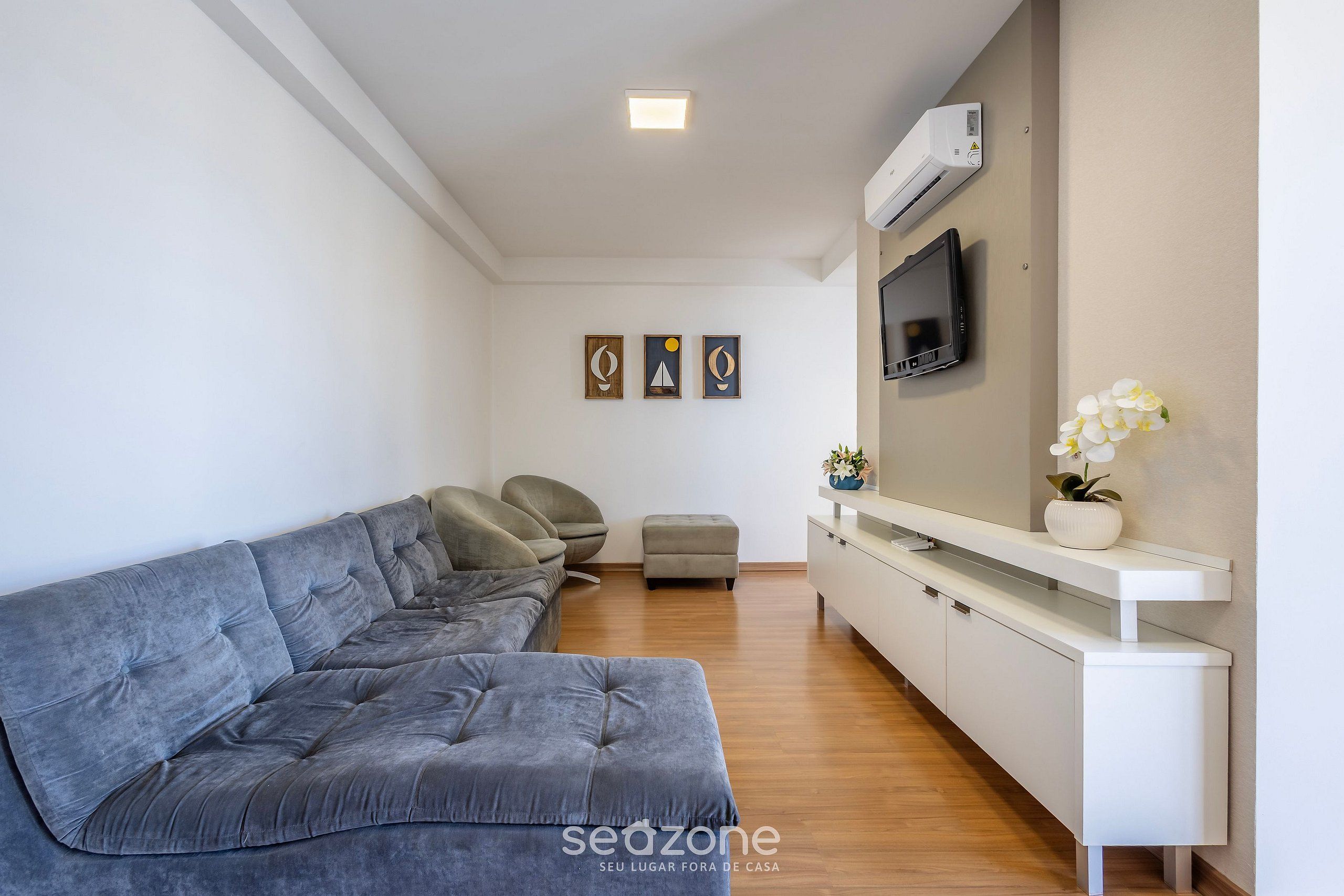 A modern living room with a grey sofa, a white console table, and a flat-screen TV mounted on the wall.
