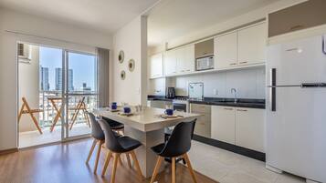 Una cocina moderna con una isla central, armarios blancos y un amplio ventanal con vistas a un paisaje urbano.