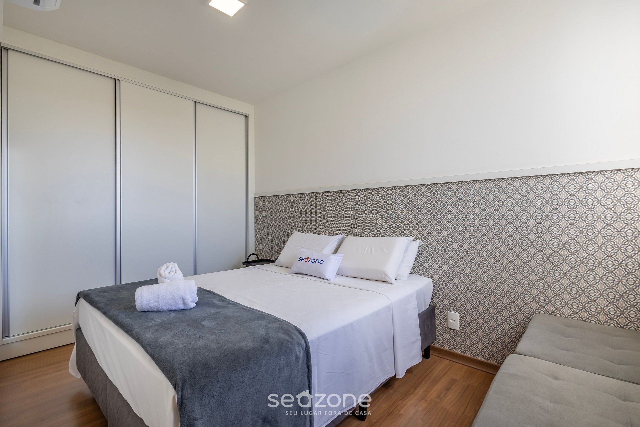 Quarto com cama, sofá, parede estampada e guarda-roupa.