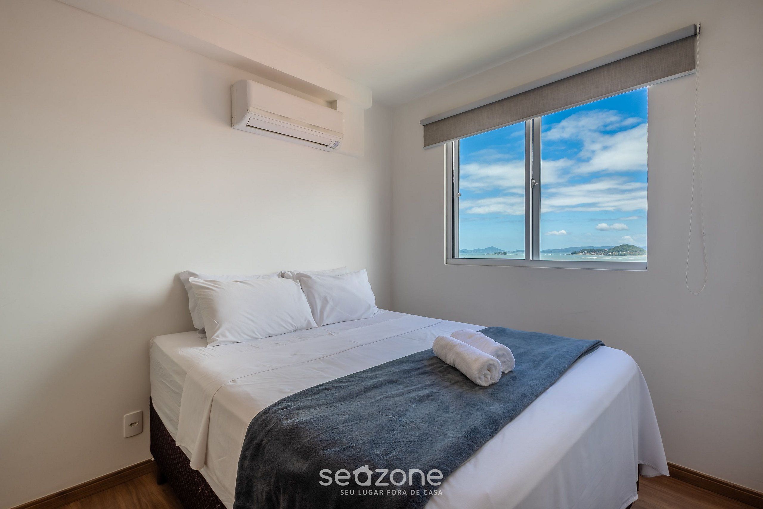 A bedroom with a bed, a window with a view, and an air conditioning unit.