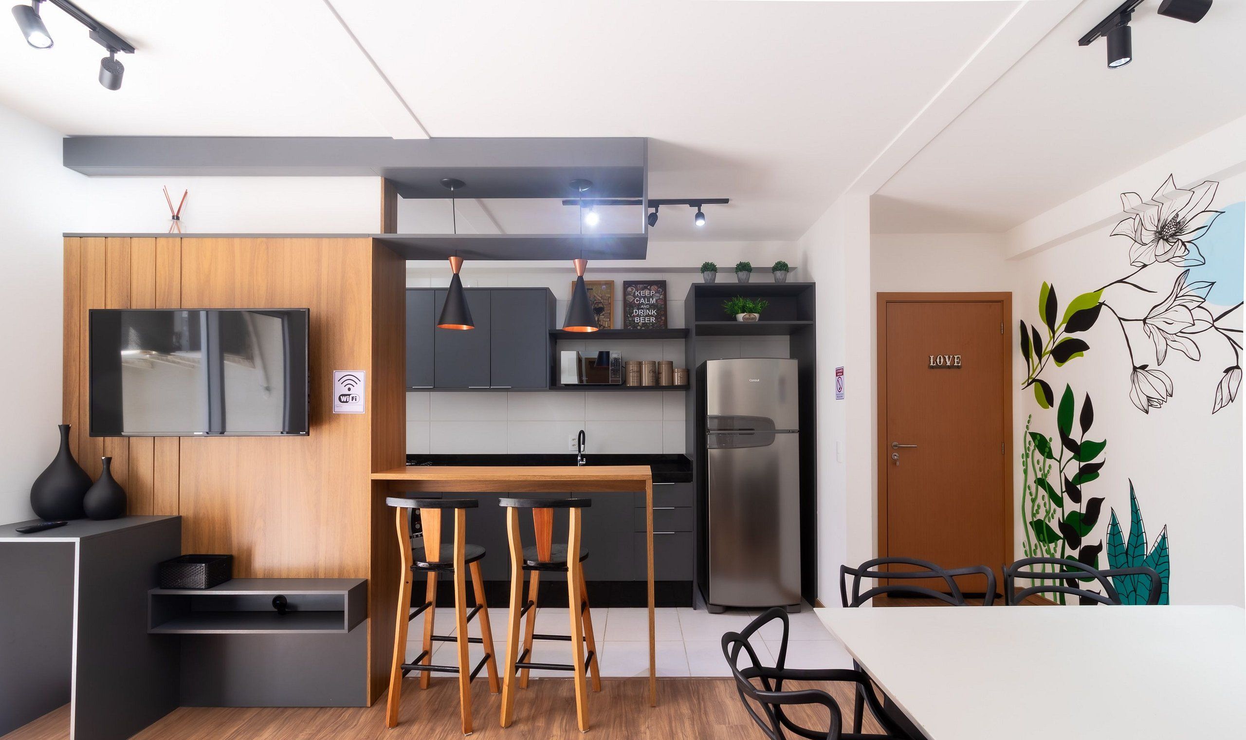 Una cocina moderna con horno empotrado, refrigerador y comedor con mesa de madera y taburetes de bar.