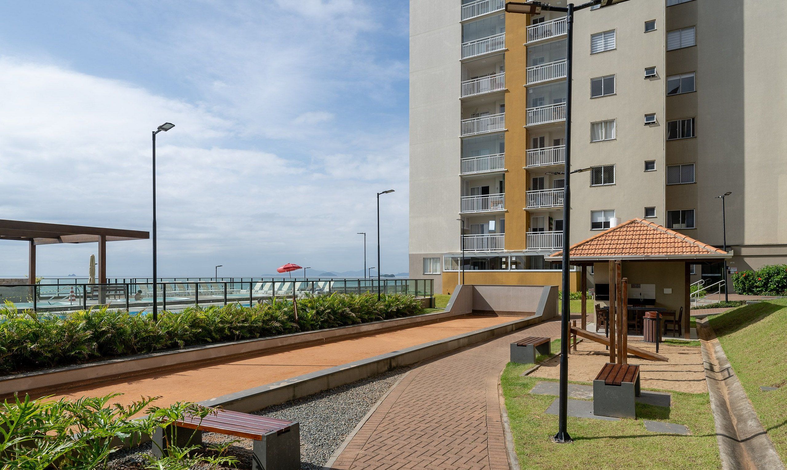 A modern apartment building with a pool area, outdoor seating, and a view of the sea.