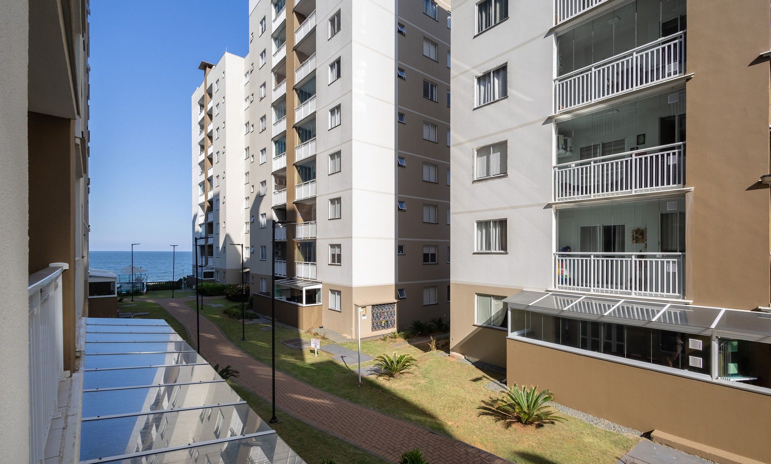 Un edificio residencial de varios pisos con balcones, un camino pavimentado y vista al mar.