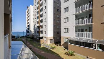 Un edificio residencial de varios pisos con balcones, un camino pavimentado y vista al mar.