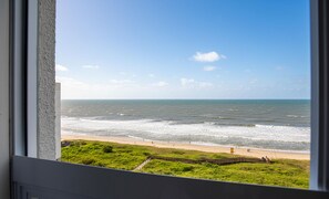 Blick auf den Ozean durch ein Fenster, im Vordergrund ein Strand und eine Wiese.