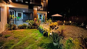 Un bâtiment à deux étages doté d’un balcon, de plantes en pot et d’un espace extérieur bien éclairé la nuit.