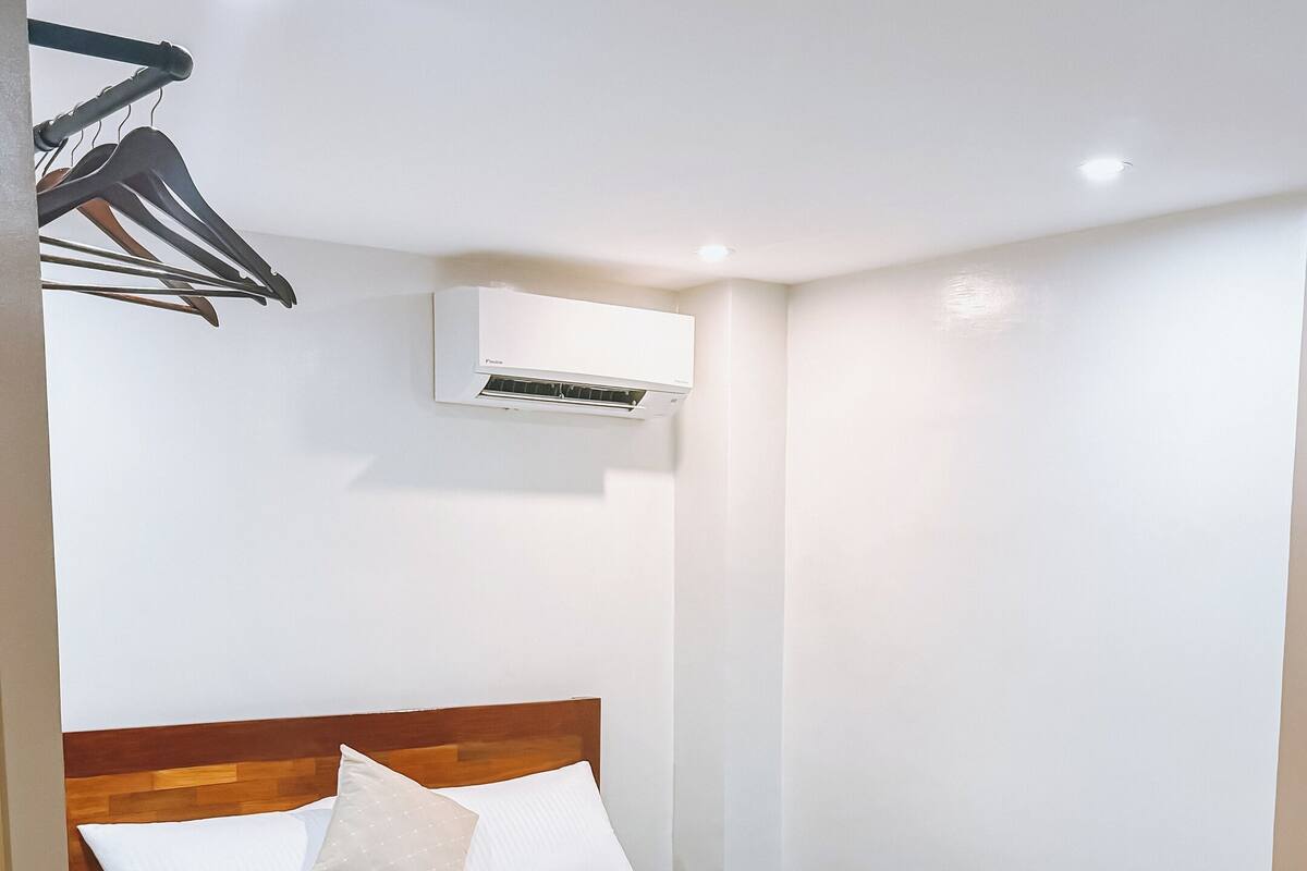 Uma cama bem arrumada com cabeceira de madeira, ar condicionado fixado na parede e piso de madeira.
