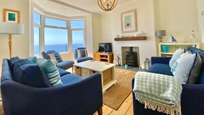 A living room with a fireplace, a television, and a large window overlooking the sea. - 83 Gills Cliff Road - Ventnor, sleeps 5 guests  in 3 bedrooms (Isle of Wight)