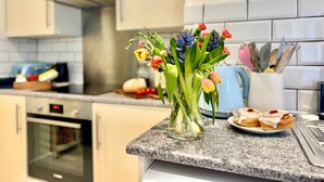 A kitchen with a granite countertop, a glass vase with flowers, a coffee maker, and a plate with pastries. - 83 Gills Cliff Road - Ventnor, sleeps 5 guests  in 3 bedrooms (Isle of Wight)