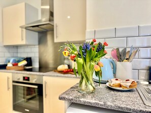 Une cuisine dotée d’un plan de travail en granit, d’un vase en verre rempli de fleurs, d’une machine à café et d’une assiette de pâtisseries.