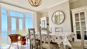A dining area with a table set for four, surrounded by chairs, a chandelier, and a view of the outdoors. - 83 Gills Cliff Road - Ventnor, sleeps 5 guests  in 3 bedrooms (Isle of Wight)