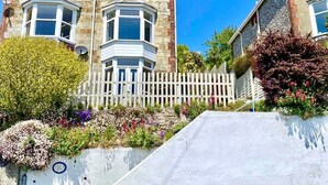 A two-story stone house with a bay window, a white picket fence, and a variety of flowering plants. - 83 Gills Cliff Road - Ventnor, sleeps 5 guests  in 3 bedrooms (Isle of Wight)
