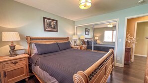 A bedroom with a wooden bed, two bedside tables with lamps, a nightstand, a mirror, and a framed picture on the wall. - Spacious/Clean 4 Bedroom 2 Bathroom Home away from Home. (Mandan)