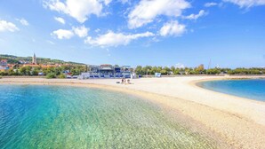 A coastal hotel with clear blue waters, a sandy beach, and a view of the town in the background. - A2 Apartment With Terrace, 1 min Walk to the Beach (Supetar)