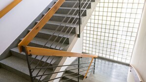 A staircase with a wooden handrail and metal balusters, leading to a lower floor. - soom Salzburg I Capsule Hotel (Salzburg)