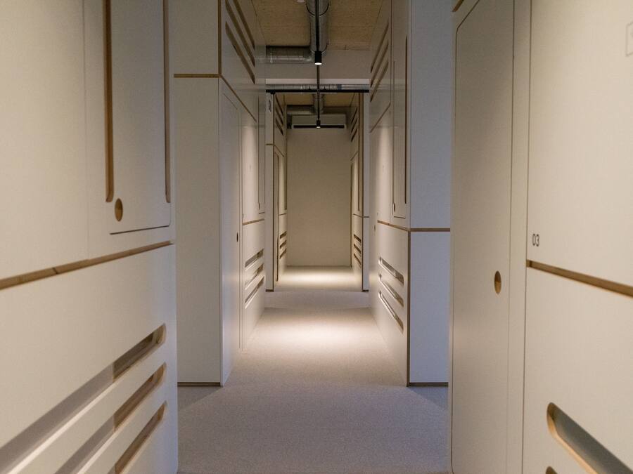 Un couloir étroit et bien éclairé, avec des portes de chaque côté, qui mène à des pièces individuelles.