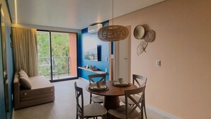 A dining area with a round table, chairs, and a window with curtains. - Mar de Campas (Tamandaré)