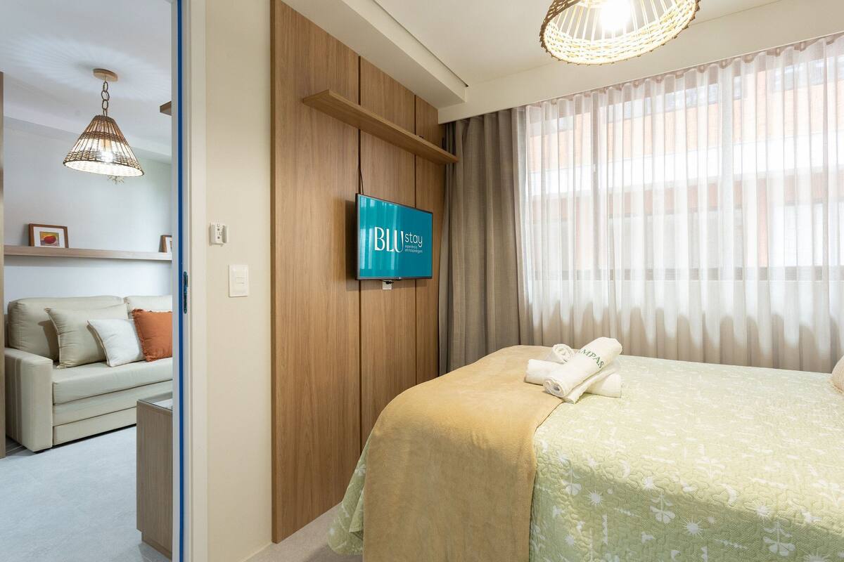 Ein Hotelzimmer mit einem Bett, einem an der Wand montierten Fernseher, einer Couch und einer Wandverkleidung aus Holz.