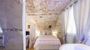 Ein Schlafzimmer mit Steindecke, einem großen Bett, einer Badewanne und einer Duschkabine.
