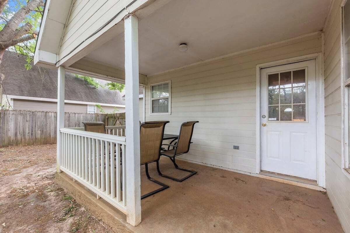 A covered porch with a white railing, a table with chairs, and a door.