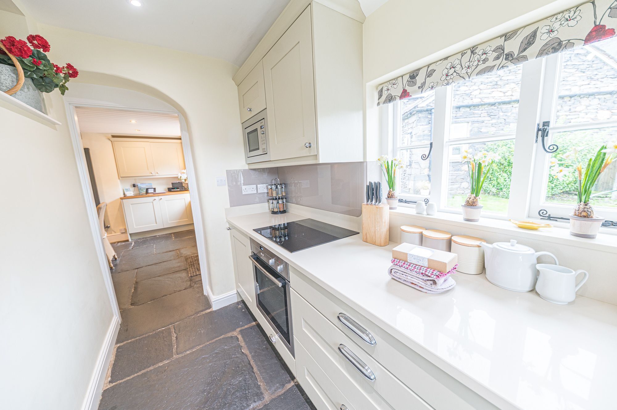 A kitchen with white cabinets, a black stove, and a window with floral curtains.