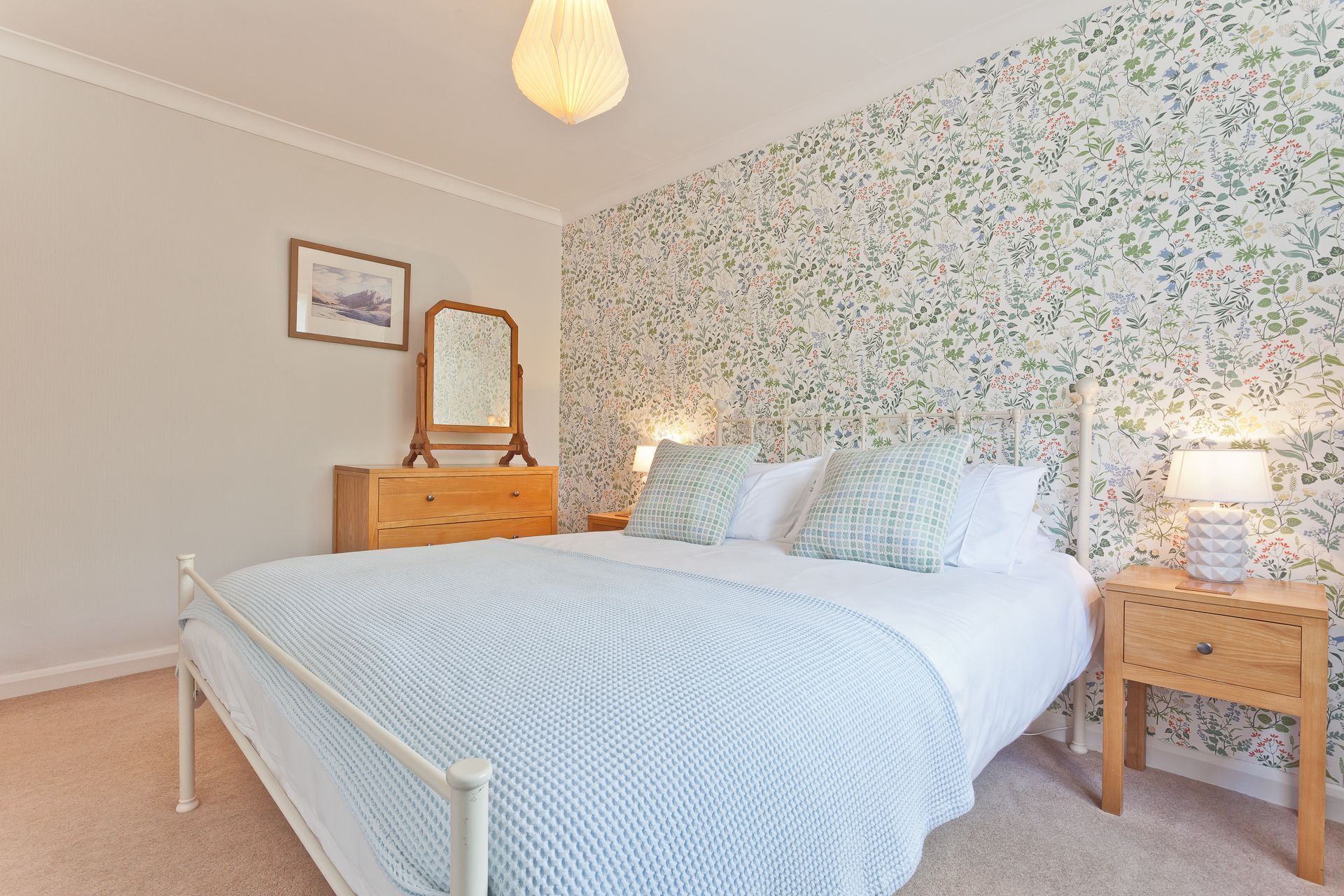 Une chambre à coucher comprenant un lit, des tables de chevet, une commode, un miroir et un papier peint à motifs floraux.