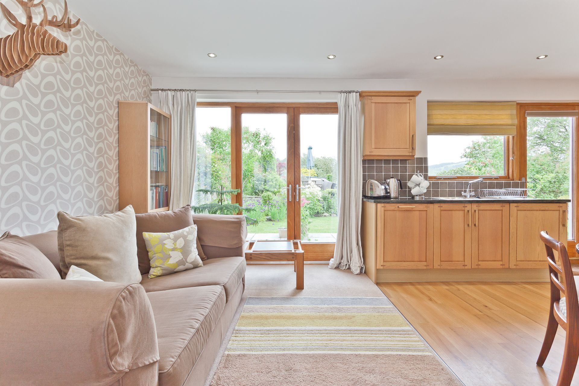 A modern living room with a sofa, a coffee table, and a view of a garden through large windows.