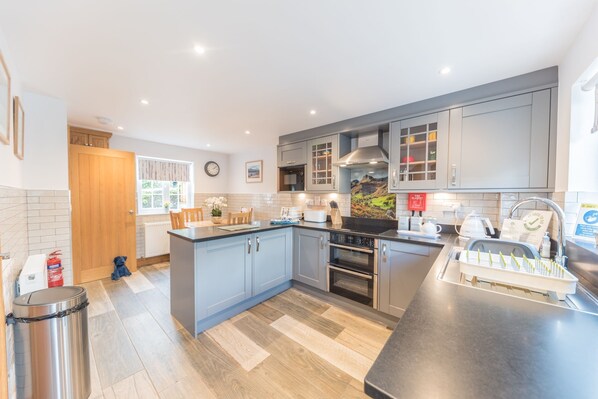 A modern kitchen with grey cabinets, a central island, a built-in oven, and a stainless steel sink.