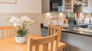 A modern kitchen with a wooden dining table, a potted orchid, and a view of the island and appliances.