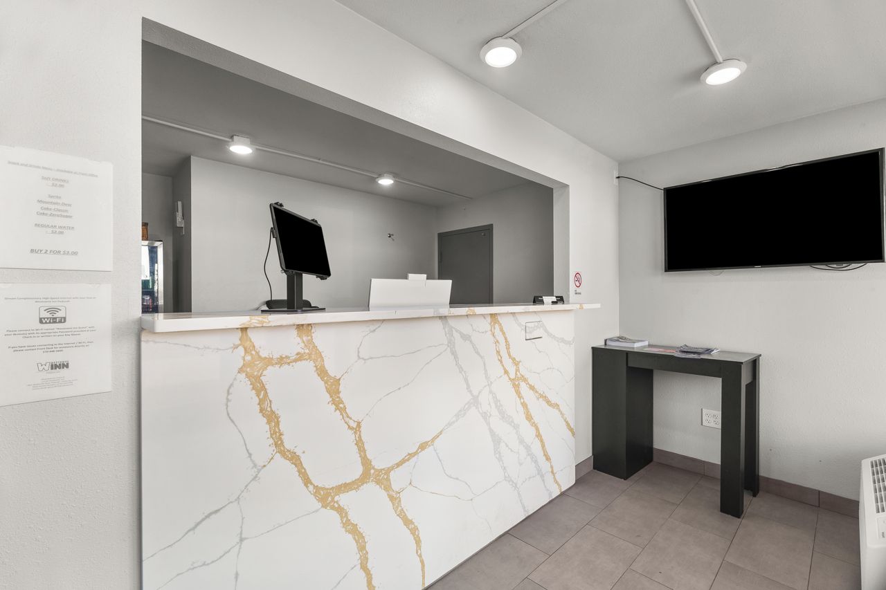 A reception desk with a marble design, a flat-screen TV mounted on the wall, and a small table with a book.