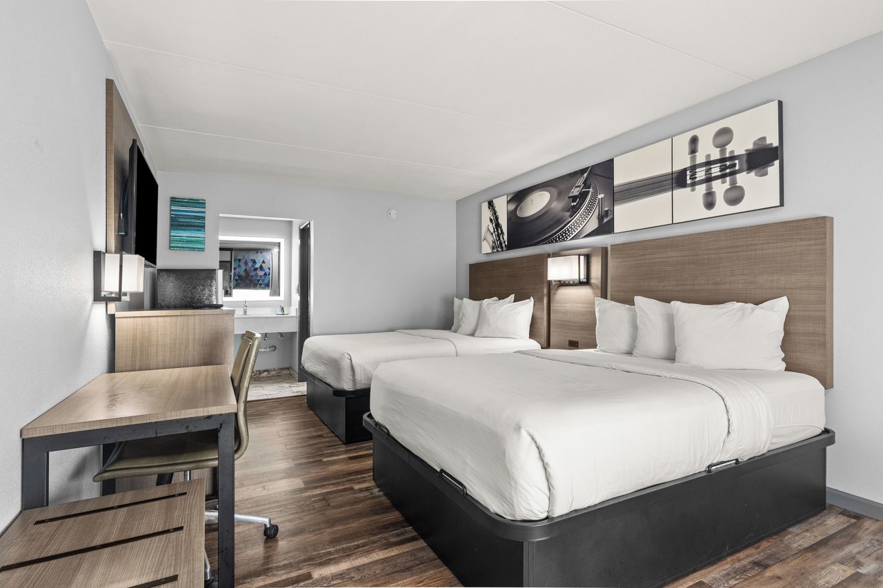 Habitació d'hotel amb escriptori, dos llits i obra d'art a la paret.