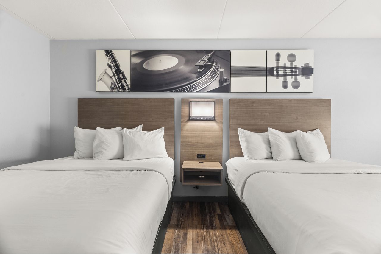 A hotel room with two beds, a wooden headboard, a nightstand, and a wall-mounted artwork.