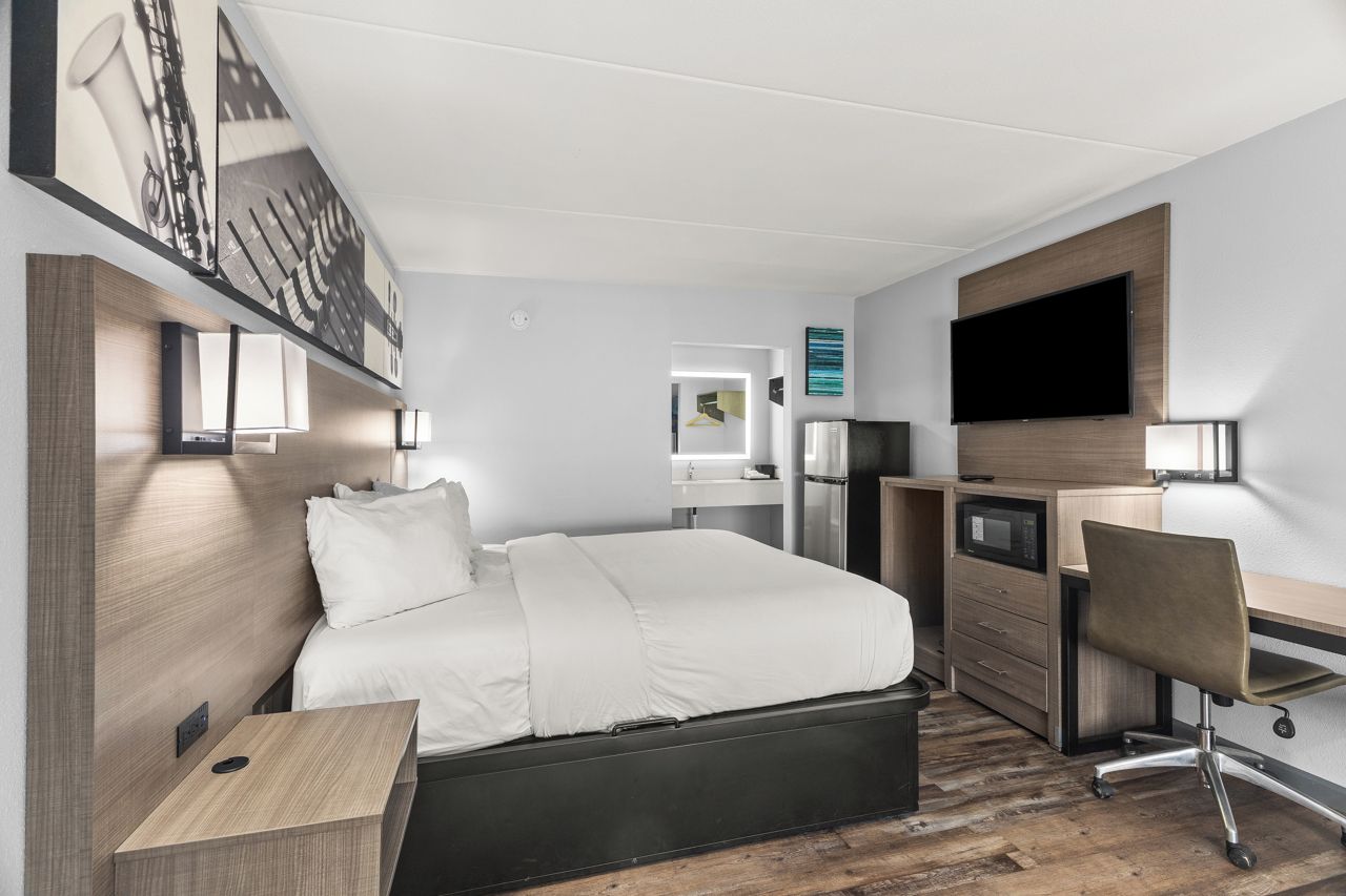 A modern hotel room with a bed, desk, chair, and a flat-screen TV.