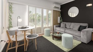 A modern living room with a grey sofa, a round mirror, and a dining area with a table and chairs.