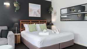 A hotel room with a large bed, a wooden headboard, a bedside table, a chair, and a wall-mounted mirror.